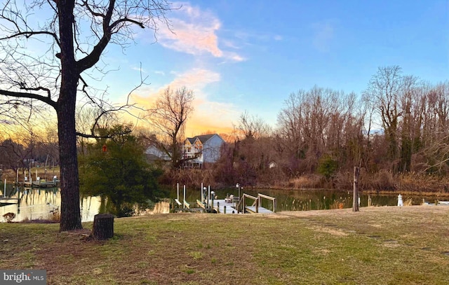 yard at dusk featuring a water view, a boat dock, and boat lift