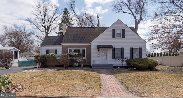 view of front of property with a front lawn, roof with shingles, and fence