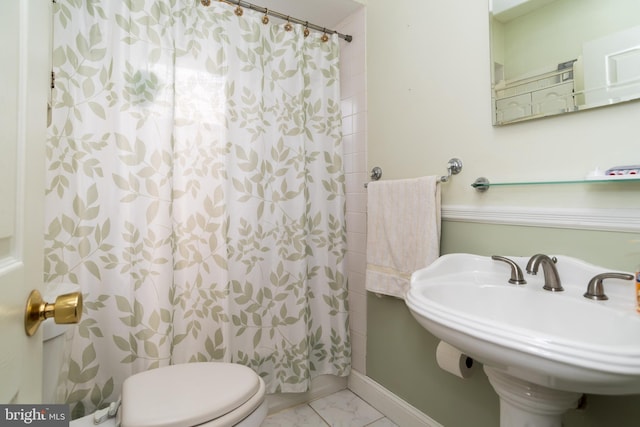 bathroom featuring marble finish floor, a shower with shower curtain, toilet, a sink, and baseboards