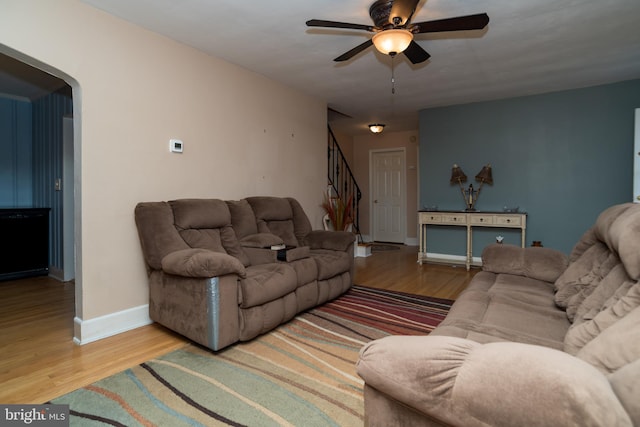 living room featuring arched walkways, wood finished floors, a ceiling fan, baseboards, and stairs