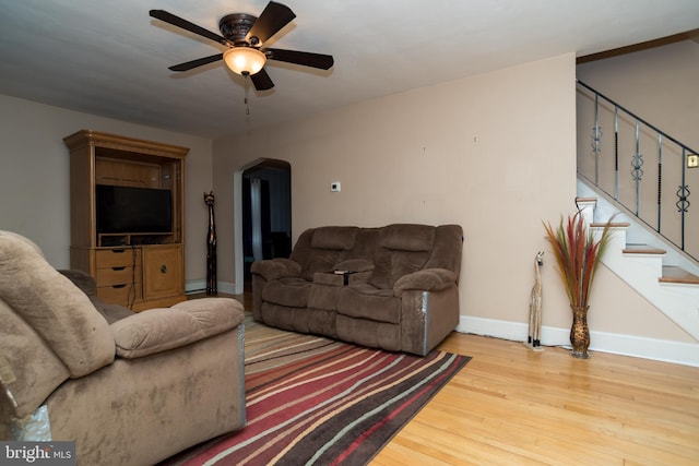 living room featuring arched walkways, stairway, ceiling fan, wood finished floors, and baseboards