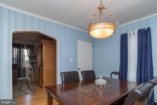 dining space featuring arched walkways, crown molding, and wood finished floors