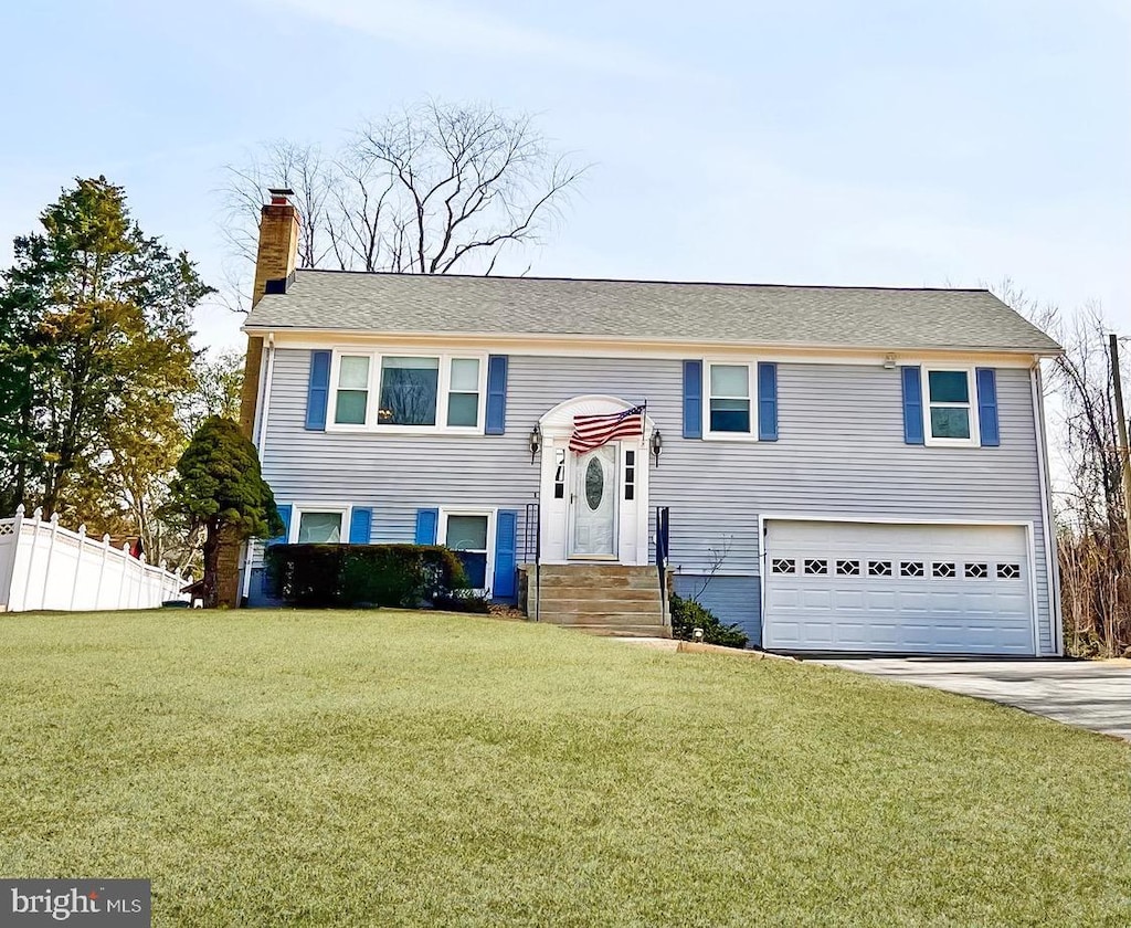 split foyer home with an attached garage, fence, driveway, a front lawn, and a chimney