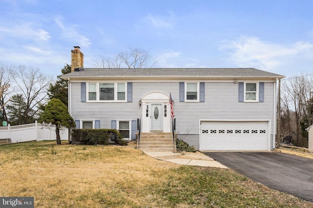 raised ranch with driveway, fence, a front yard, a garage, and a chimney