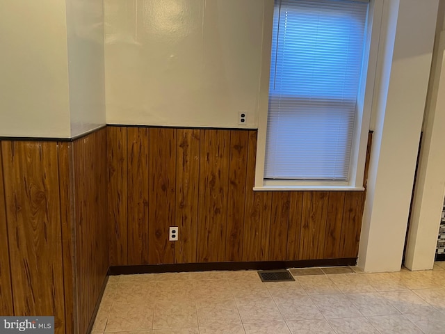 empty room featuring wainscoting, visible vents, and wooden walls