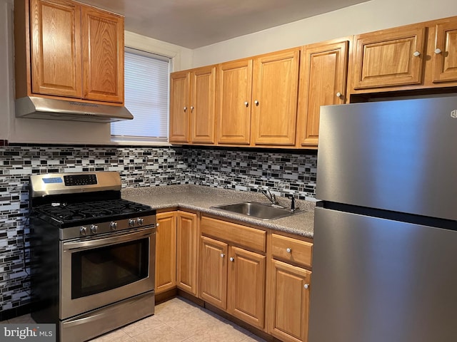 kitchen featuring light tile patterned floors, under cabinet range hood, a sink, appliances with stainless steel finishes, and decorative backsplash