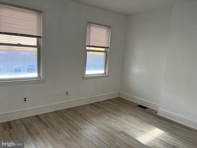 empty room featuring a wealth of natural light, wood finished floors, and visible vents