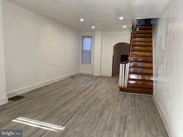 interior space featuring baseboards, arched walkways, stairway, wood finished floors, and recessed lighting