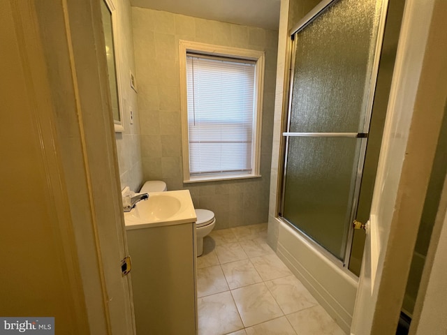 bathroom featuring tile patterned flooring, toilet, shower / bath combination with glass door, vanity, and tile walls