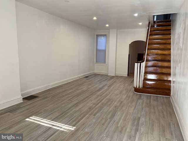 unfurnished living room featuring arched walkways, visible vents, stairway, and wood finished floors