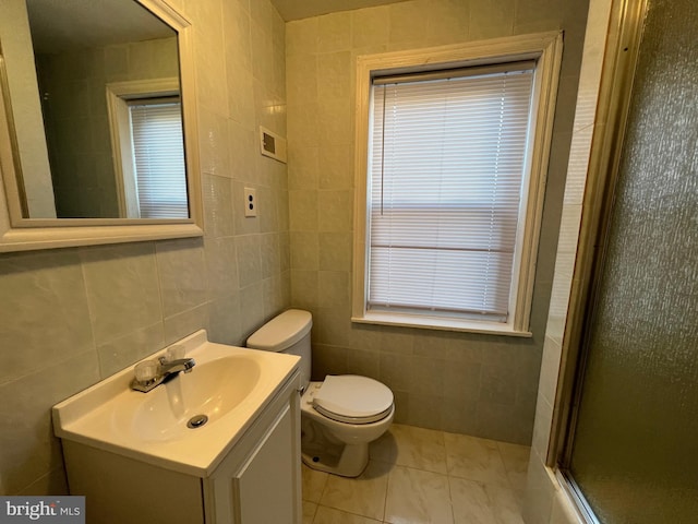 bathroom featuring toilet, a shower with shower door, tile patterned floors, vanity, and tile walls