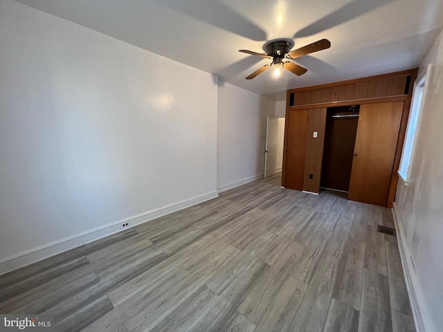 unfurnished bedroom featuring a ceiling fan, light wood-style flooring, baseboards, and a closet