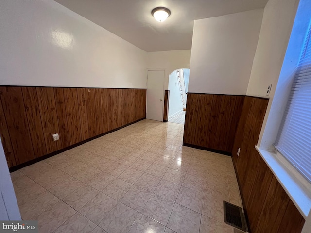 spare room featuring arched walkways, wainscoting, visible vents, and wooden walls