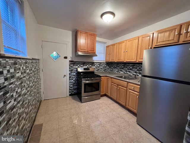 kitchen featuring light tile patterned floors, under cabinet range hood, a sink, appliances with stainless steel finishes, and decorative backsplash