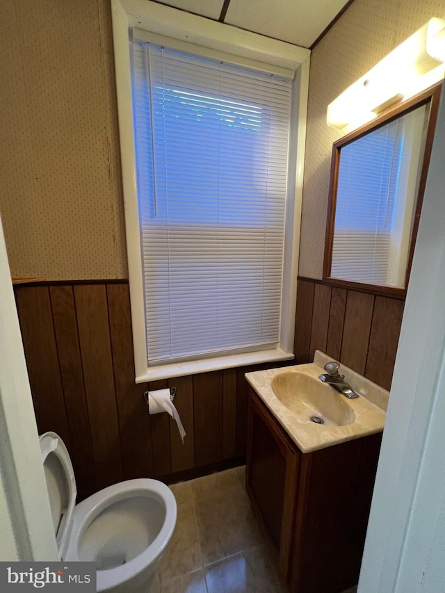 bathroom featuring toilet, a wainscoted wall, vanity, tile patterned floors, and wallpapered walls