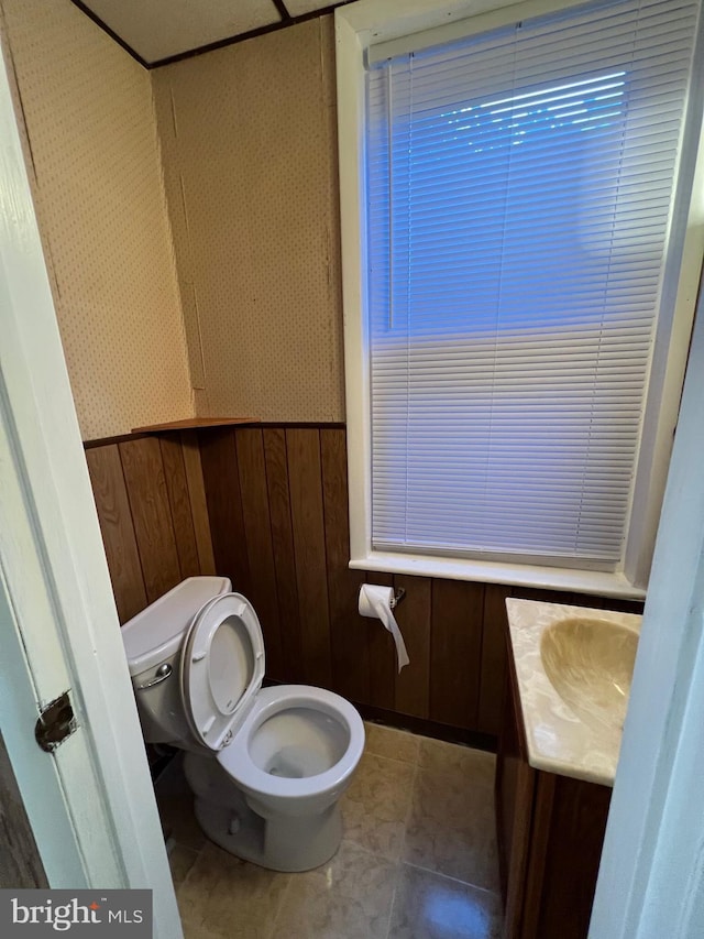 half bathroom with toilet, a wainscoted wall, tile patterned floors, vanity, and wood walls