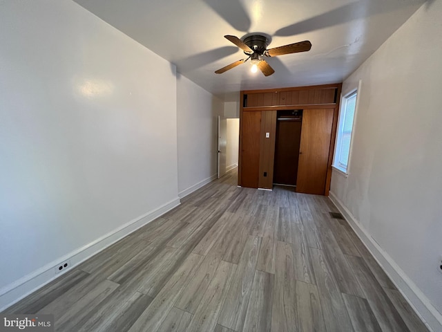 unfurnished bedroom with a closet, visible vents, a ceiling fan, wood finished floors, and baseboards