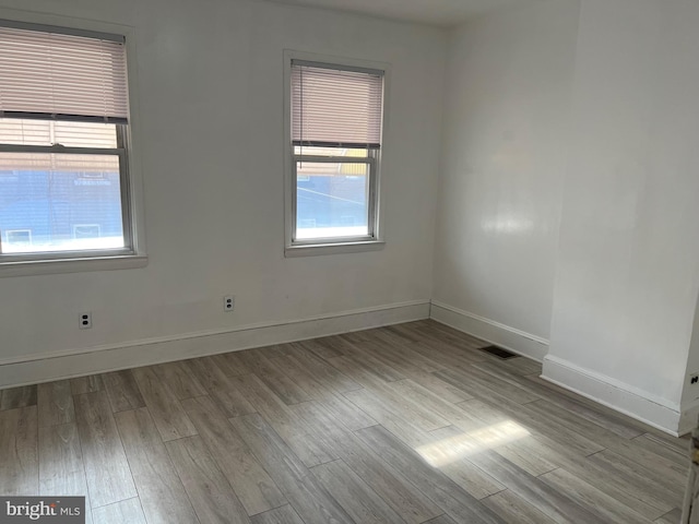 empty room with a healthy amount of sunlight, visible vents, baseboards, and wood finished floors