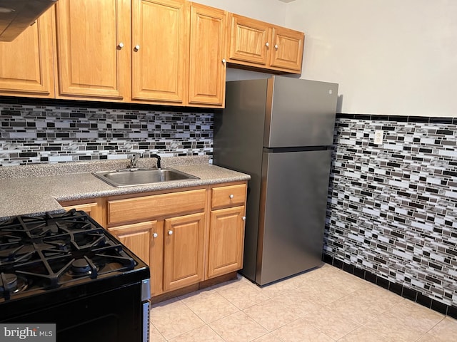 kitchen featuring light tile patterned flooring, a sink, tile walls, black range with gas stovetop, and freestanding refrigerator