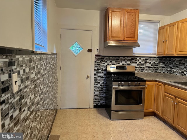 kitchen featuring tile walls, dark countertops, stainless steel range with gas stovetop, light tile patterned flooring, and under cabinet range hood