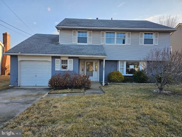 traditional-style house featuring an attached garage, a shingled roof, concrete driveway, and a front yard