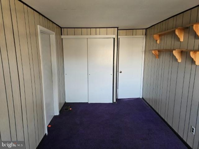 unfurnished bedroom featuring carpet floors, a closet, and wood walls