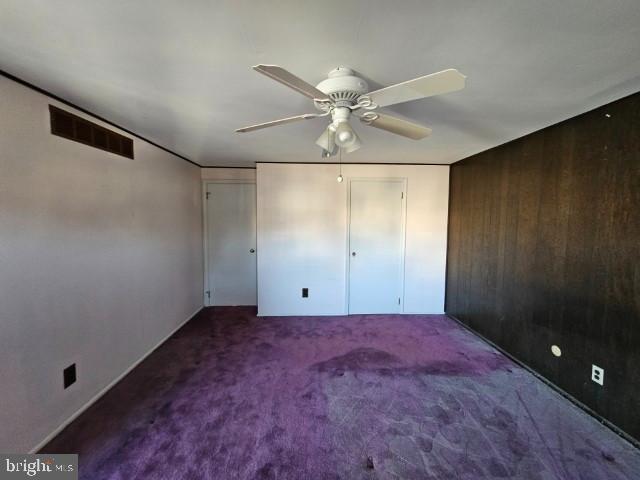 unfurnished bedroom with a ceiling fan, visible vents, wood walls, and carpet flooring