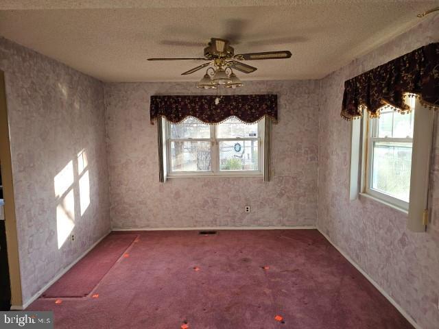 empty room with carpet floors, a ceiling fan, a textured ceiling, and wallpapered walls