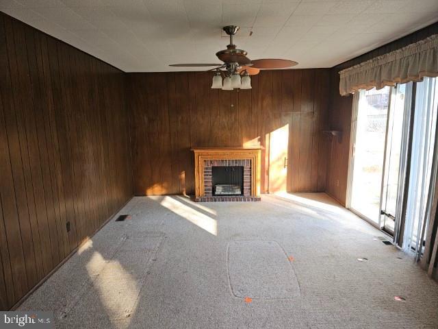 unfurnished living room featuring carpet floors, a brick fireplace, wood walls, and ceiling fan