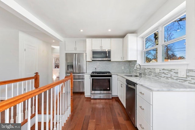 kitchen with a sink, white cabinetry, stainless steel appliances, decorative backsplash, and light stone countertops