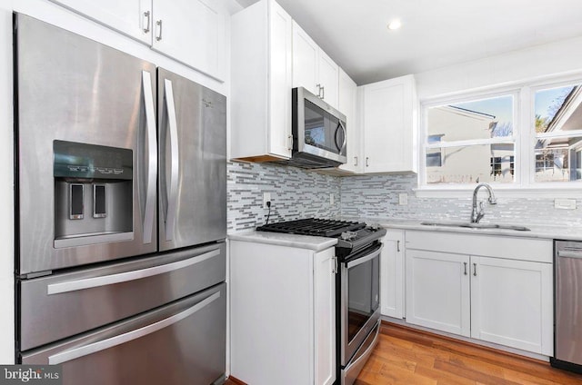 kitchen featuring light wood finished floors, a sink, decorative backsplash, appliances with stainless steel finishes, and white cabinetry