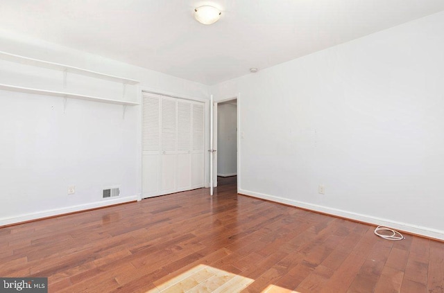 unfurnished bedroom with hardwood / wood-style floors, baseboards, visible vents, and a closet