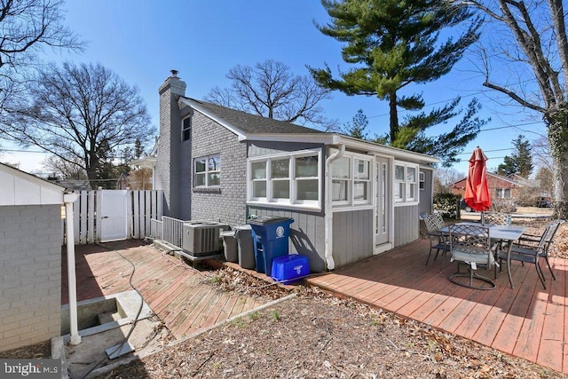 exterior space featuring a wooden deck, brick siding, outdoor dining space, and a chimney