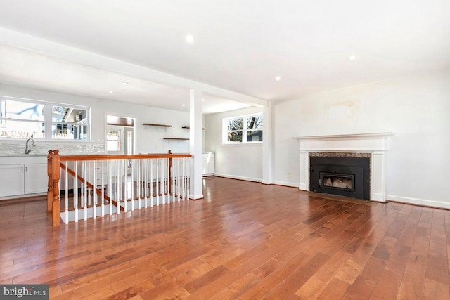 unfurnished living room with a sink, baseboards, a fireplace with flush hearth, and wood finished floors