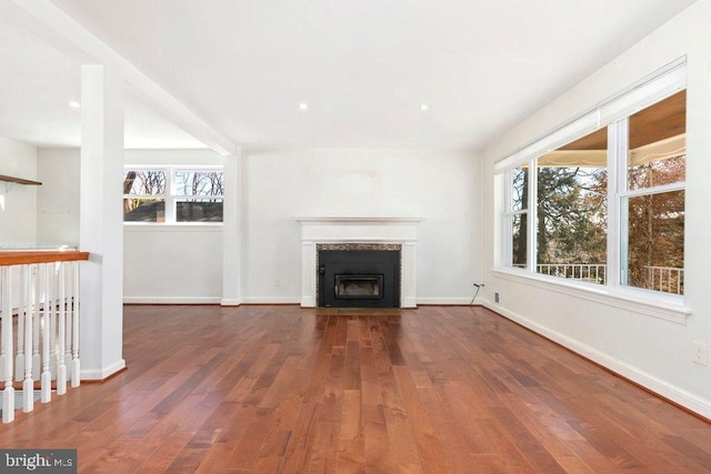 unfurnished living room featuring a wealth of natural light, a fireplace with flush hearth, baseboards, and wood finished floors