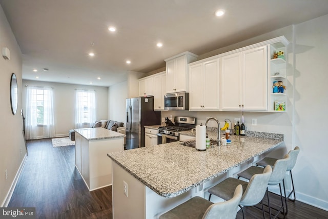 kitchen with stainless steel appliances, a sink, white cabinets, a center island, and dark wood finished floors