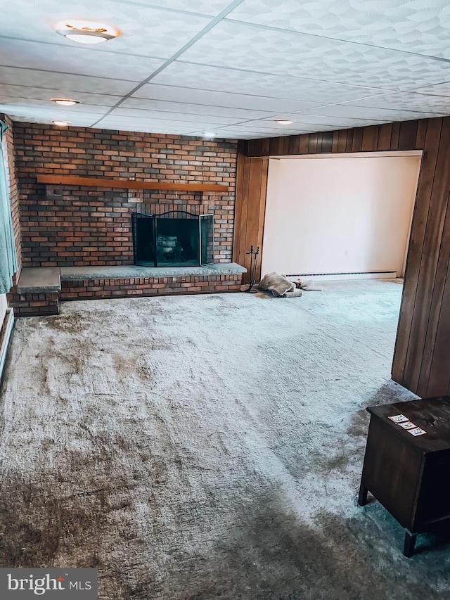 unfurnished living room with carpet floors, a fireplace, wood walls, and baseboard heating