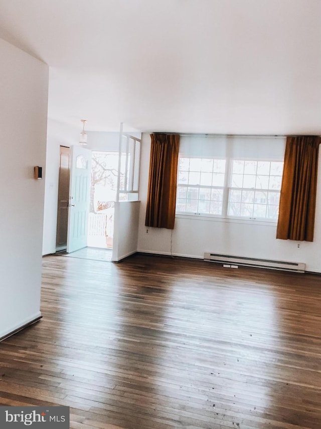 unfurnished living room featuring a baseboard heating unit, a healthy amount of sunlight, and wood finished floors