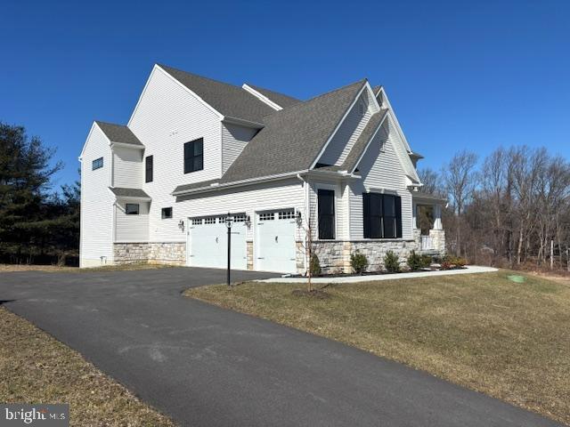 view of front facade featuring aphalt driveway, stone siding, a front lawn, and an attached garage