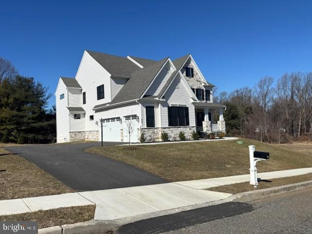 view of front facade featuring a front lawn, stone siding, driveway, and an attached garage