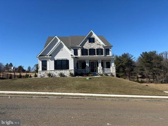 craftsman-style home featuring stone siding, a front lawn, and covered porch