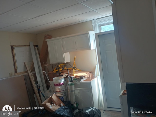 interior space with a drop ceiling and white cabinets