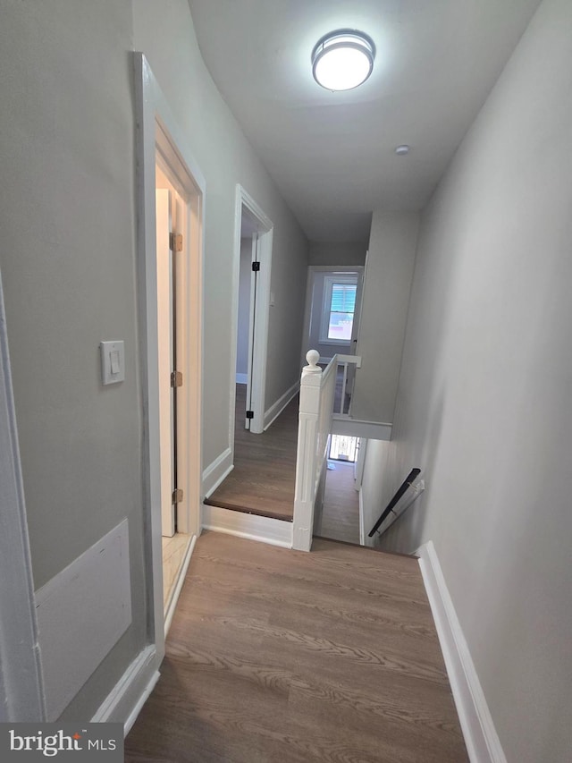 corridor with baseboards, an upstairs landing, and wood finished floors