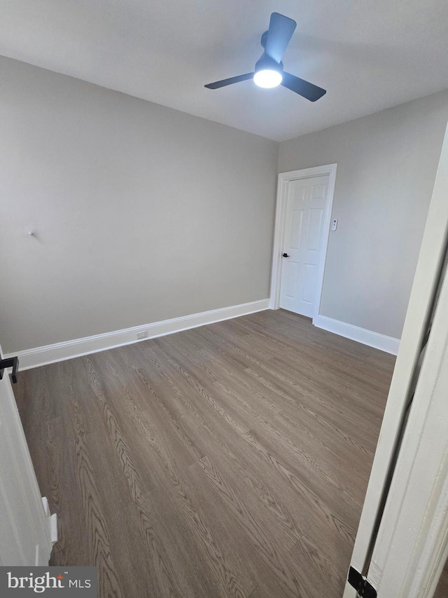 empty room with ceiling fan, dark wood-type flooring, and baseboards