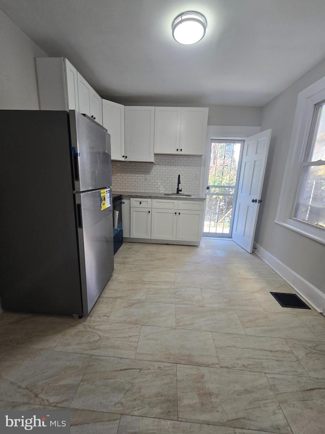 kitchen with a wealth of natural light, a sink, freestanding refrigerator, and white cabinetry