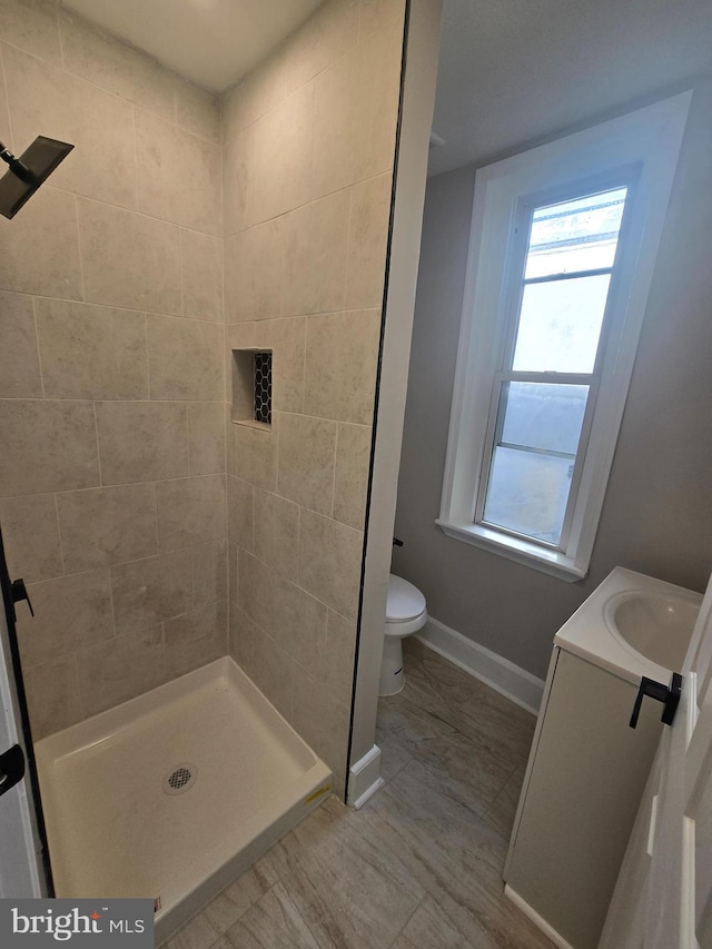 bathroom with toilet, a stall shower, baseboards, and vanity