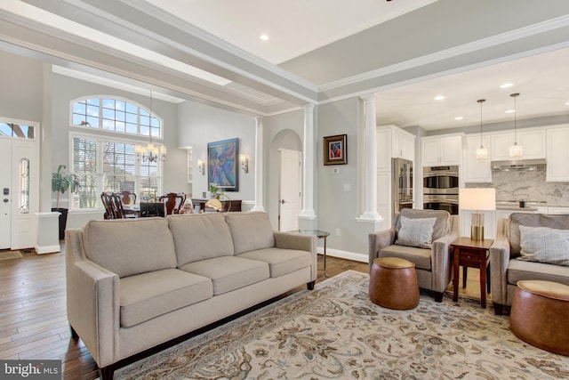 living room featuring decorative columns, baseboards, wood-type flooring, ornamental molding, and an inviting chandelier