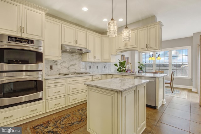 kitchen with under cabinet range hood, stainless steel appliances, a sink, cream cabinetry, and tasteful backsplash