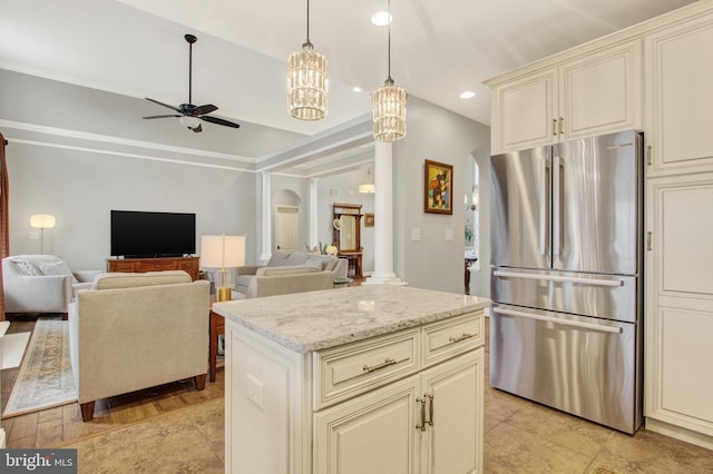 kitchen featuring light stone counters, arched walkways, cream cabinetry, a ceiling fan, and freestanding refrigerator