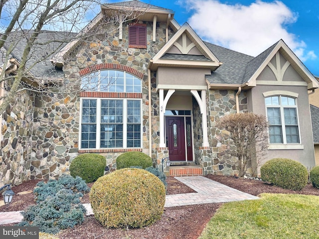 view of front of house featuring stone siding, a shingled roof, and stucco siding